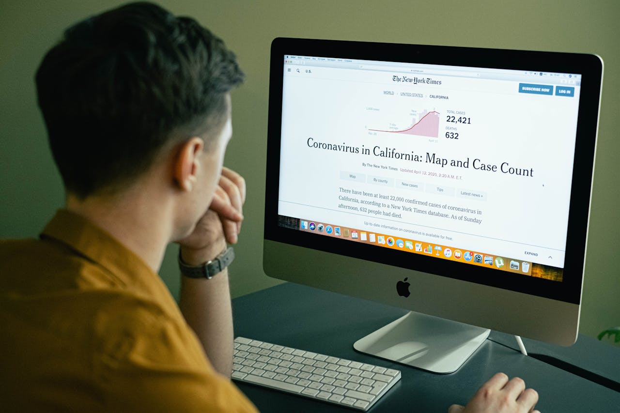 A man reading a coronavirus case count article on a computer screen indoors.